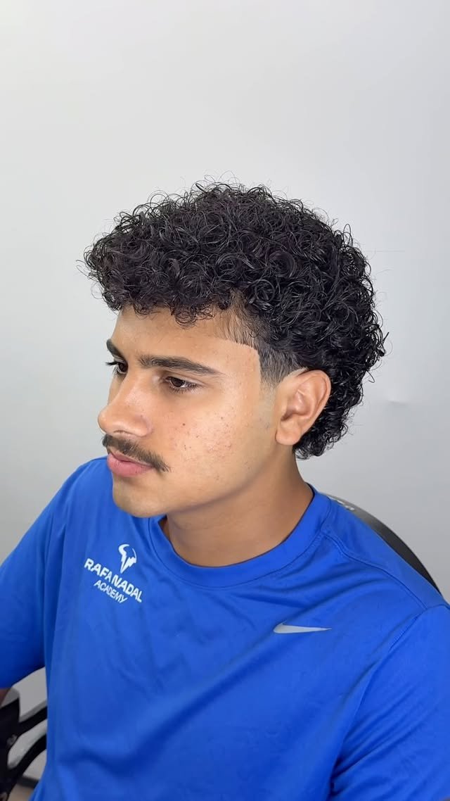 Client showing a finished modern mullet with curly top and clean taper on the sides